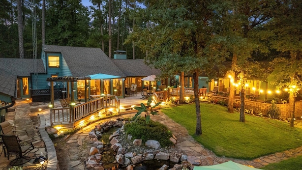A two-story house with a stone patio, outdoor seating, and string lights. - Sleeps 15 | Private custom pool | Hot Tub on 7 Secluded Acres (Holly Lake Ranch)