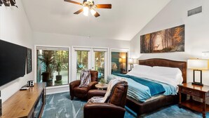 A spacious bedroom with a large bed, a ceiling fan, a TV, and a painting of a forest scene. - Sleeps 15 | Private custom pool | Hot Tub on 7 Secluded Acres (Holly Lake Ranch)