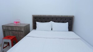 A bed with a tufted headboard, a wooden nightstand with a drawer, and a red stool. - Ratana Cengkareng (Jakarta)
