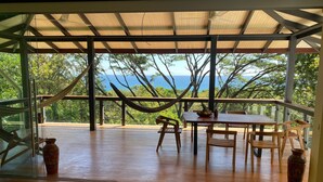 Une terrasse en bois avec une table et des chaises, un hamac et une vue sur l’océan.