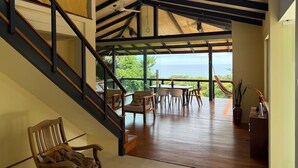 Un intérieur spacieux avec un escalier en bois menant à un balcon d’où l’on a une vue sur l’océan.