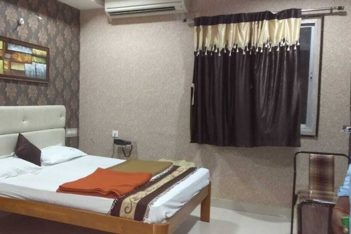 Ein Schlafzimmer mit Bett, Nachttisch, Wandairconditioner und einem Fenster mit Vorhängen.