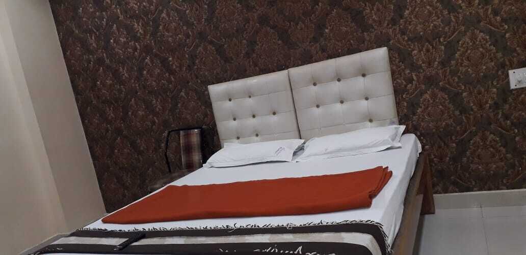 A neatly made bed with a white headboard and a red blanket, set against a patterned wallpaper.