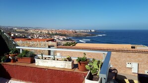 Et kystlandskab med bygninger med terracotta-tag, en klar blå himmel og udsigt til havet.