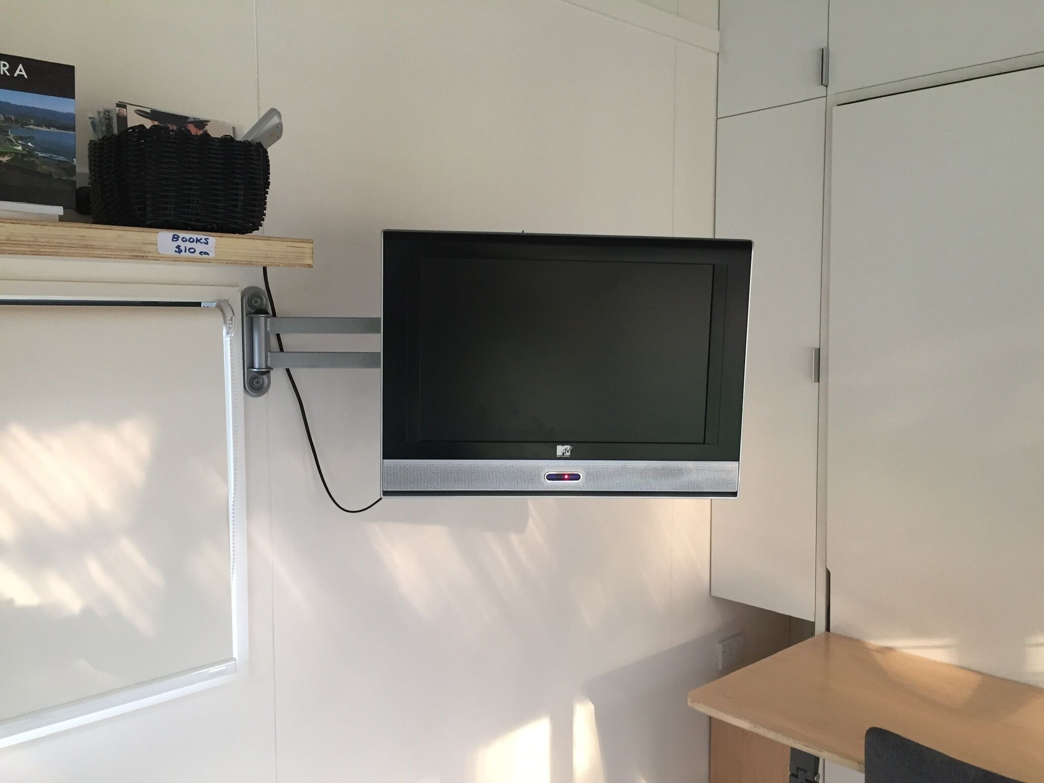 Un televisor de pantalla plana montado en la pared, con un estante superior que contiene libros y una cesta.