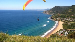 Un paysage côtier avec une plage, une personne pratiquant le parapente et une ville en arrière-plan.