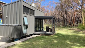 Un bâtiment moderne en métal gris, doté d’une porte en verre et d’un espace extérieur abrité avec des sièges.