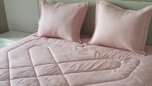 Ein Bett mit einer gesteppten rosa Tagesdecke und zwei Kissen.
