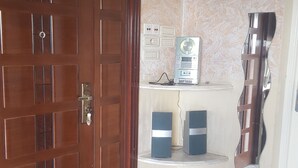Ein Zimmer mit Holztür, Marmorboden, einer Uhr, Steckdosen und zwei Lautsprechern auf einem Regal.