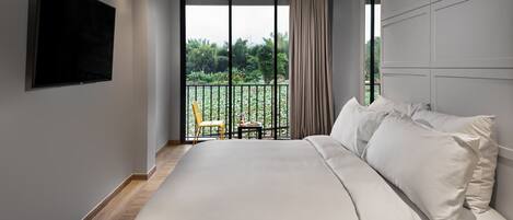 Une chambre moderne dotée d’un grand lit, d’un téléviseur à écran plat et d’un balcon offrant une vue sur la verdure.