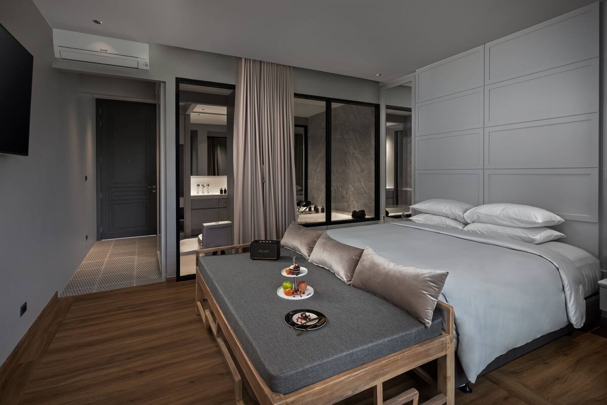 A modern hotel room with a large bed, a small seating area with a table, and a bathroom visible through an open door.