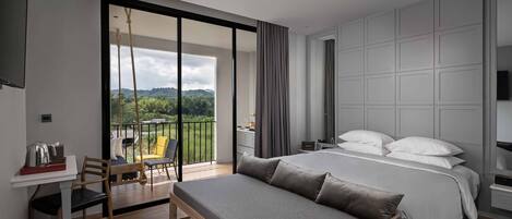 Habitación de hotel moderna con una cama grande, un escritorio y un balcón con vistas a zonas verdes.