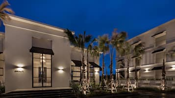 A modern hotel with a white facade, a glass entrance, and palm trees in the foreground.