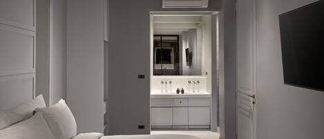 A modern bedroom with a large bed, a white vanity with a mirror, and a flat-screen TV mounted on the wall.