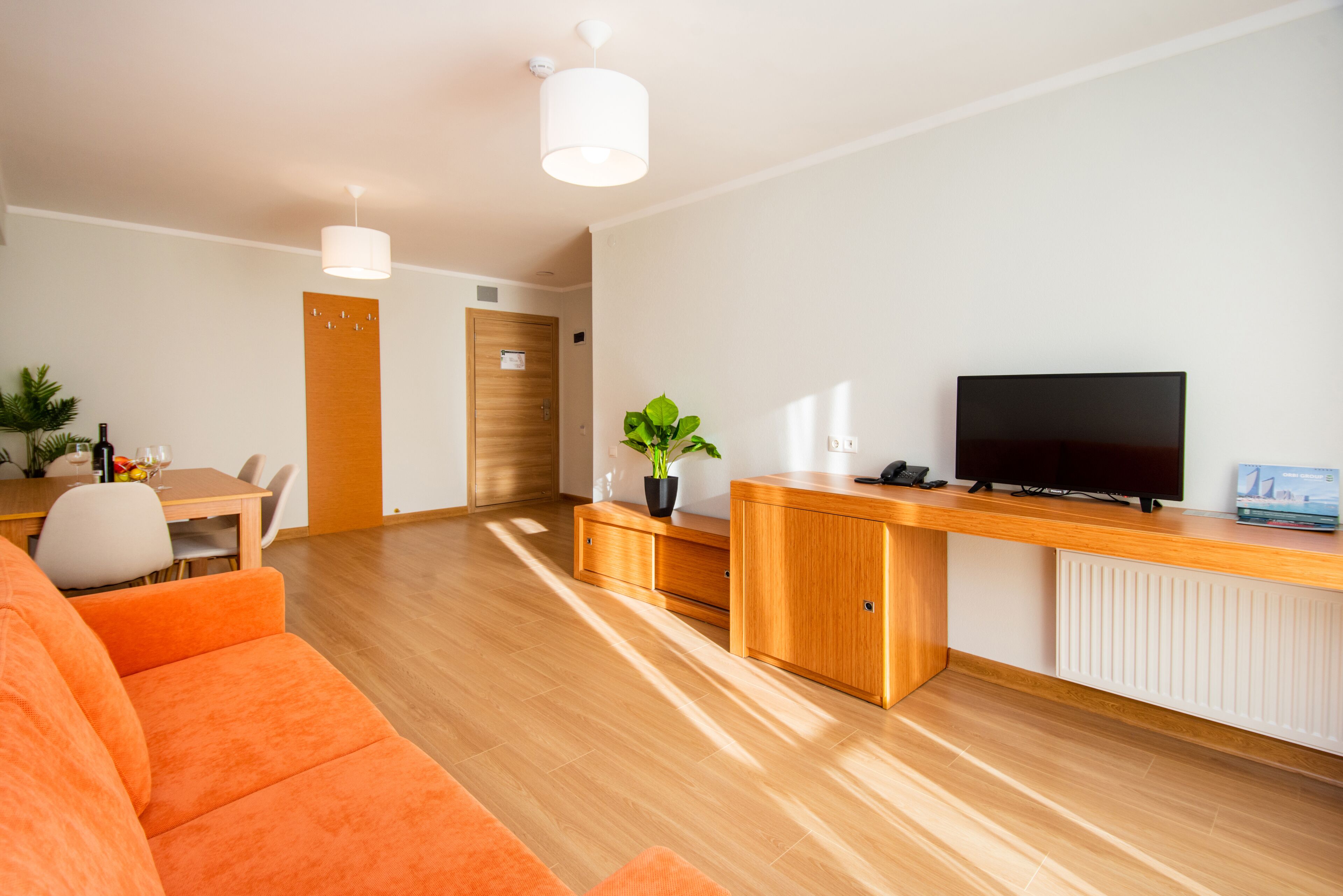 Una sala de estar moderna con una mesa de centro de madera, sofá naranja y un televisor sobre un mueble de madera.
