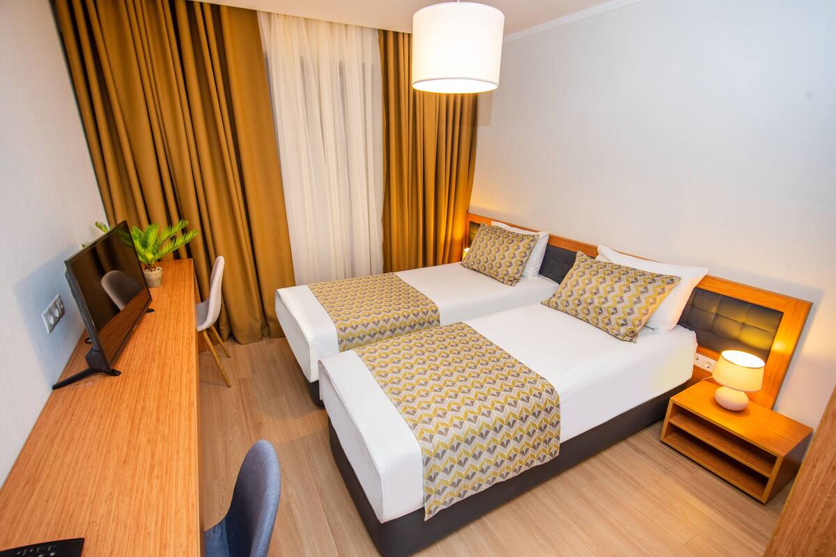 A hotel room with two beds, a desk, a chair, a lamp, and a plant.