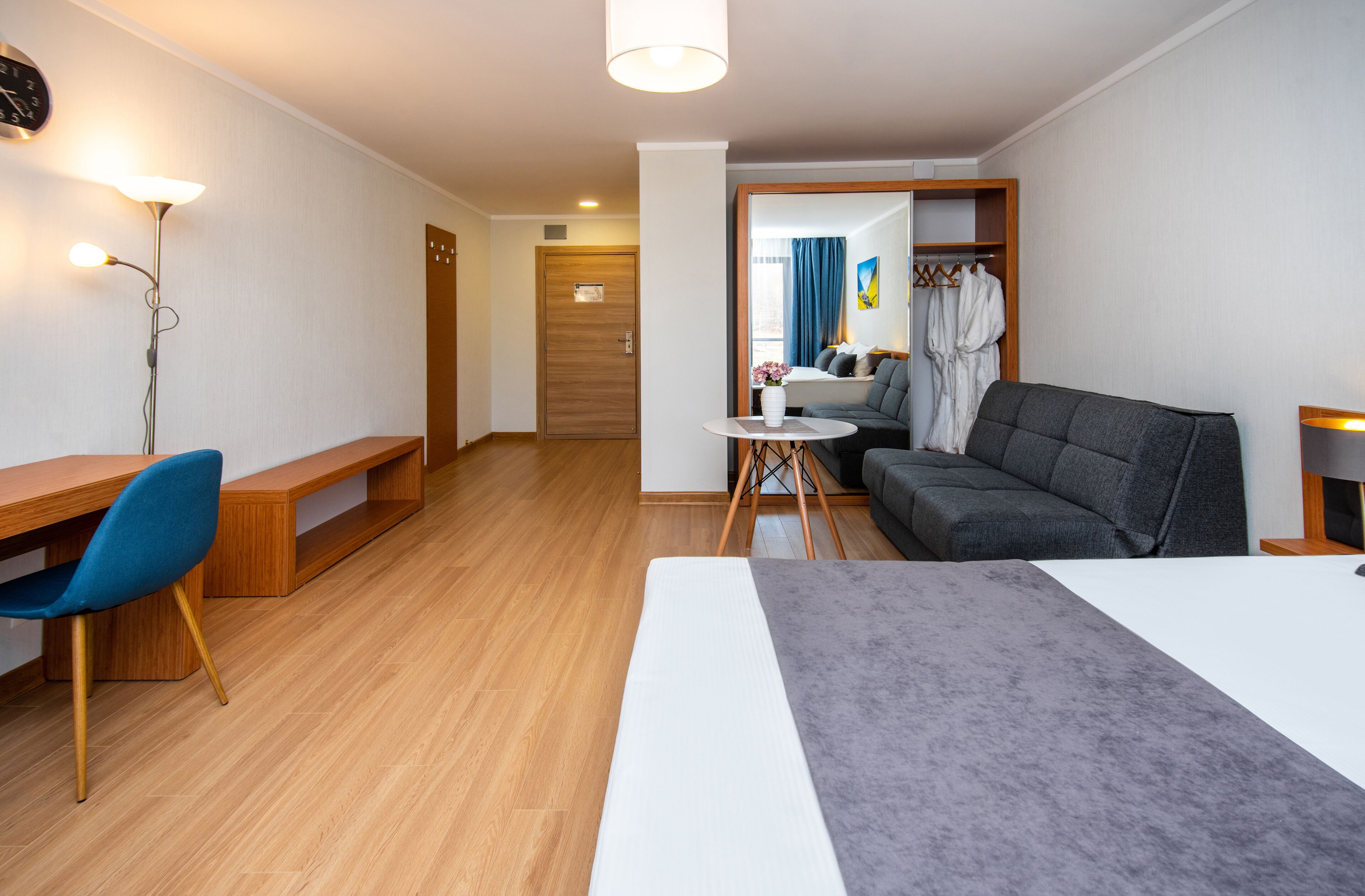 A hotel room with a bed, a desk, a chair, a sofa, a small table, and a wardrobe.