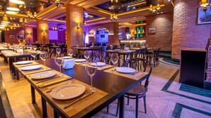 A restaurant with long tables set for dining, a bar area, and brick walls.
