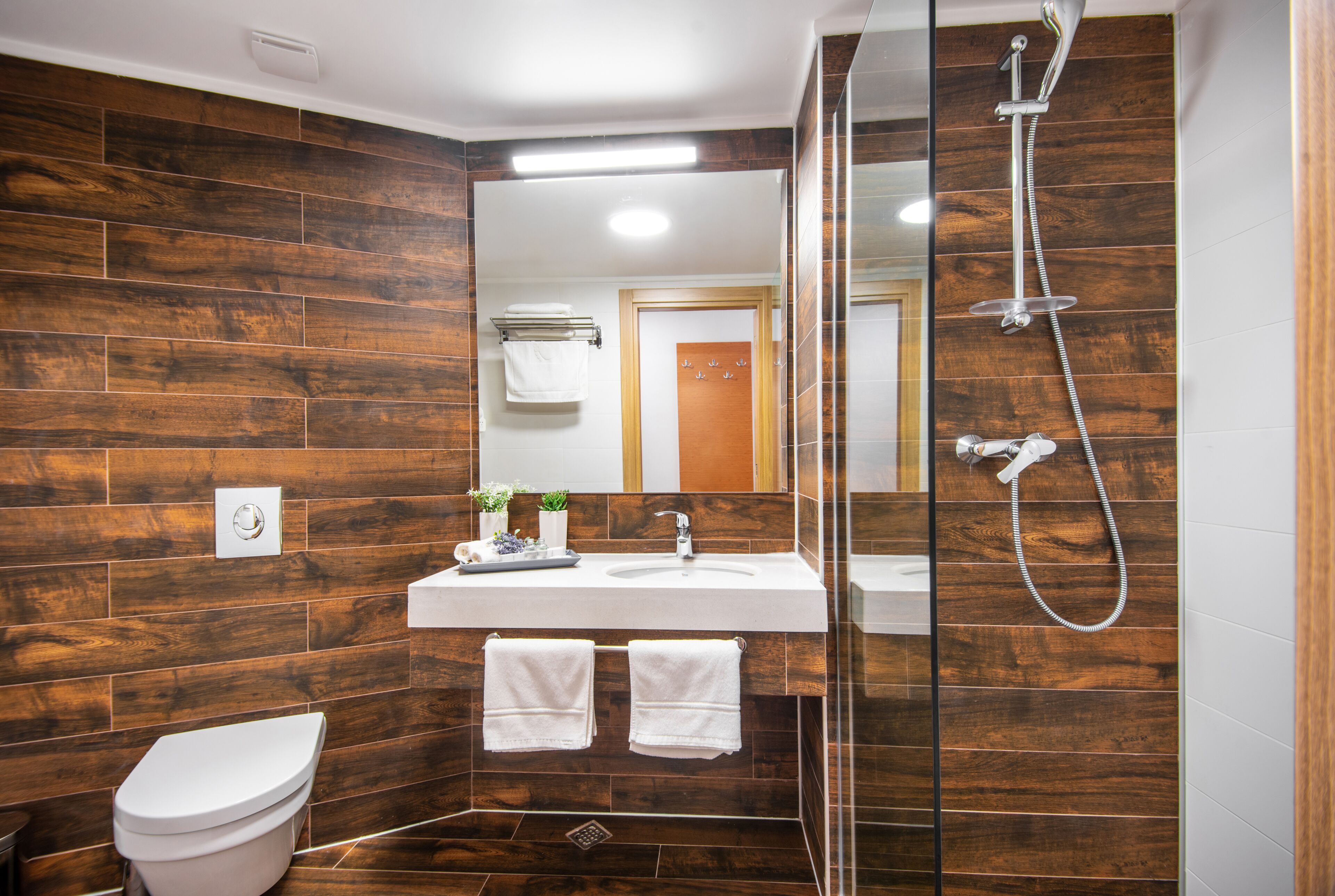 A modern bathroom with a wooden wall design, a glass shower enclosure, a white sink, and a toilet.