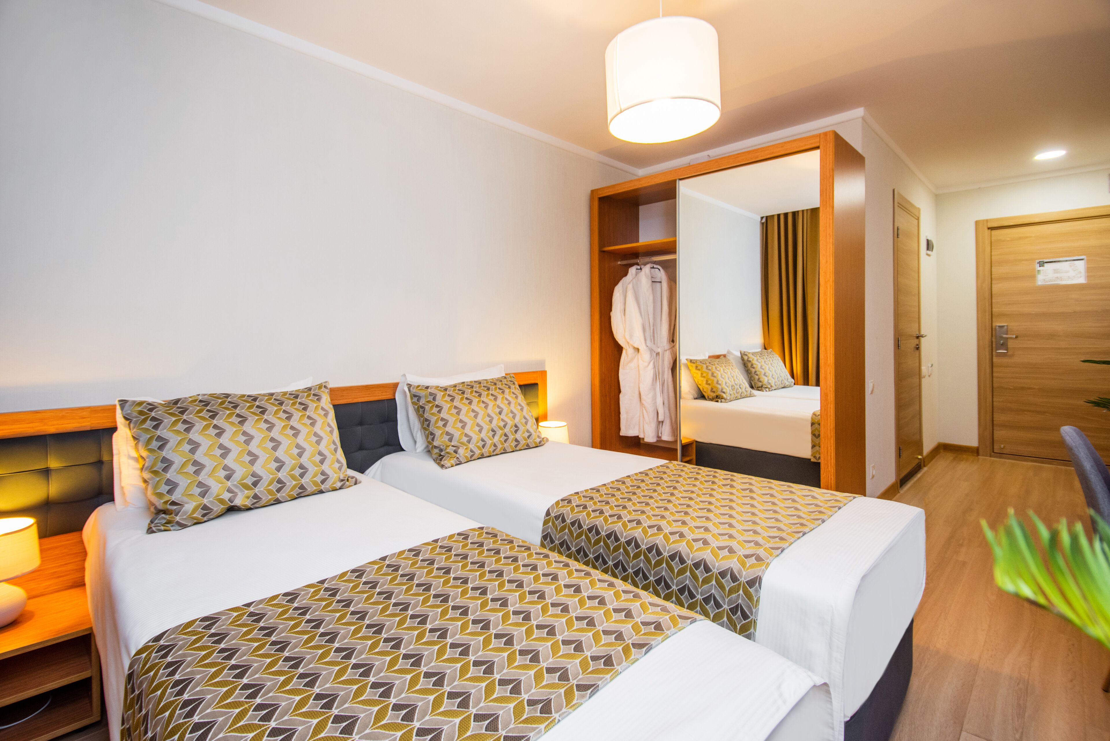 A hotel room with two beds, a wardrobe, a mirror, and a plant.