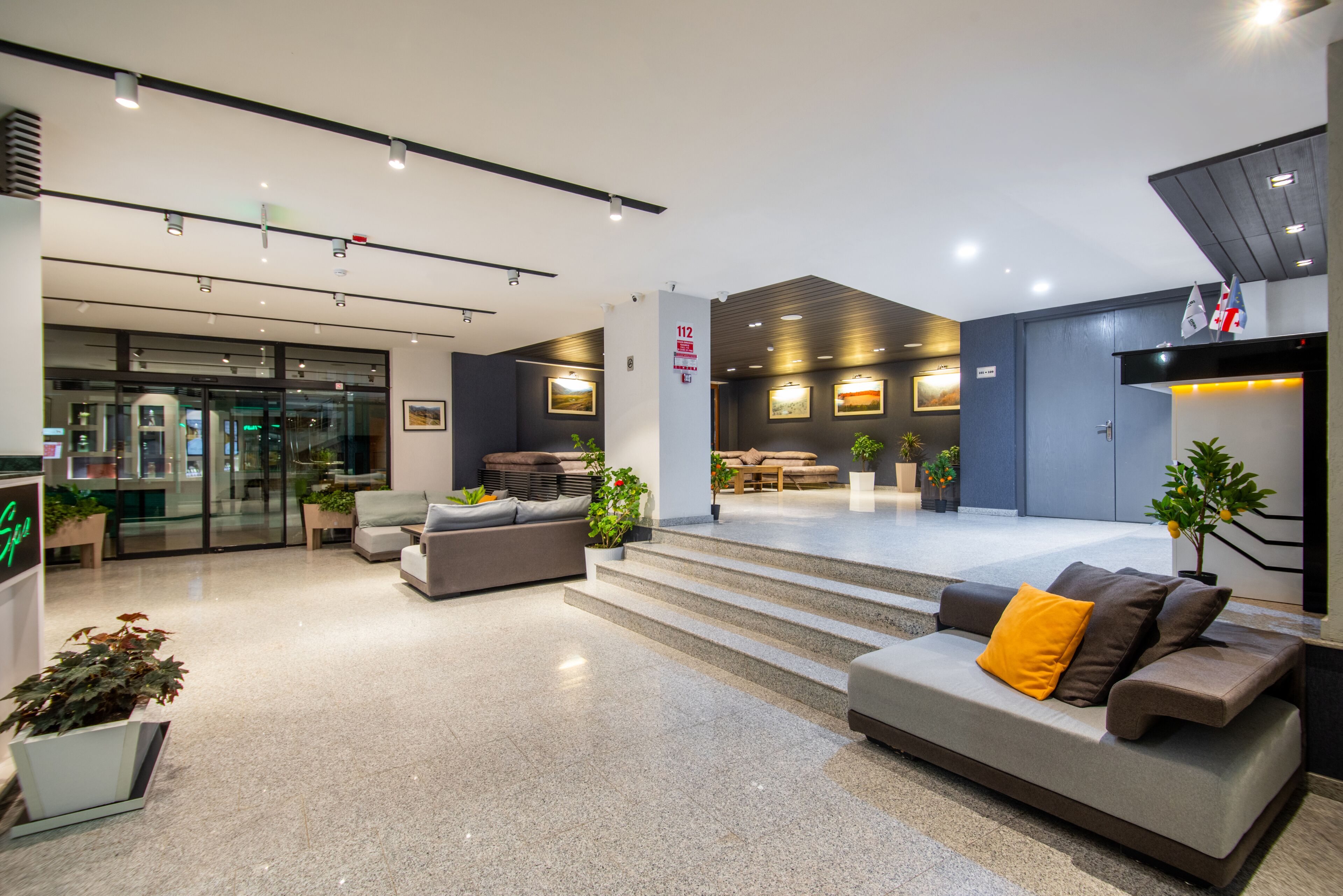 A modern lobby with a reception desk, seating area, and a staircase leading to upper floors.