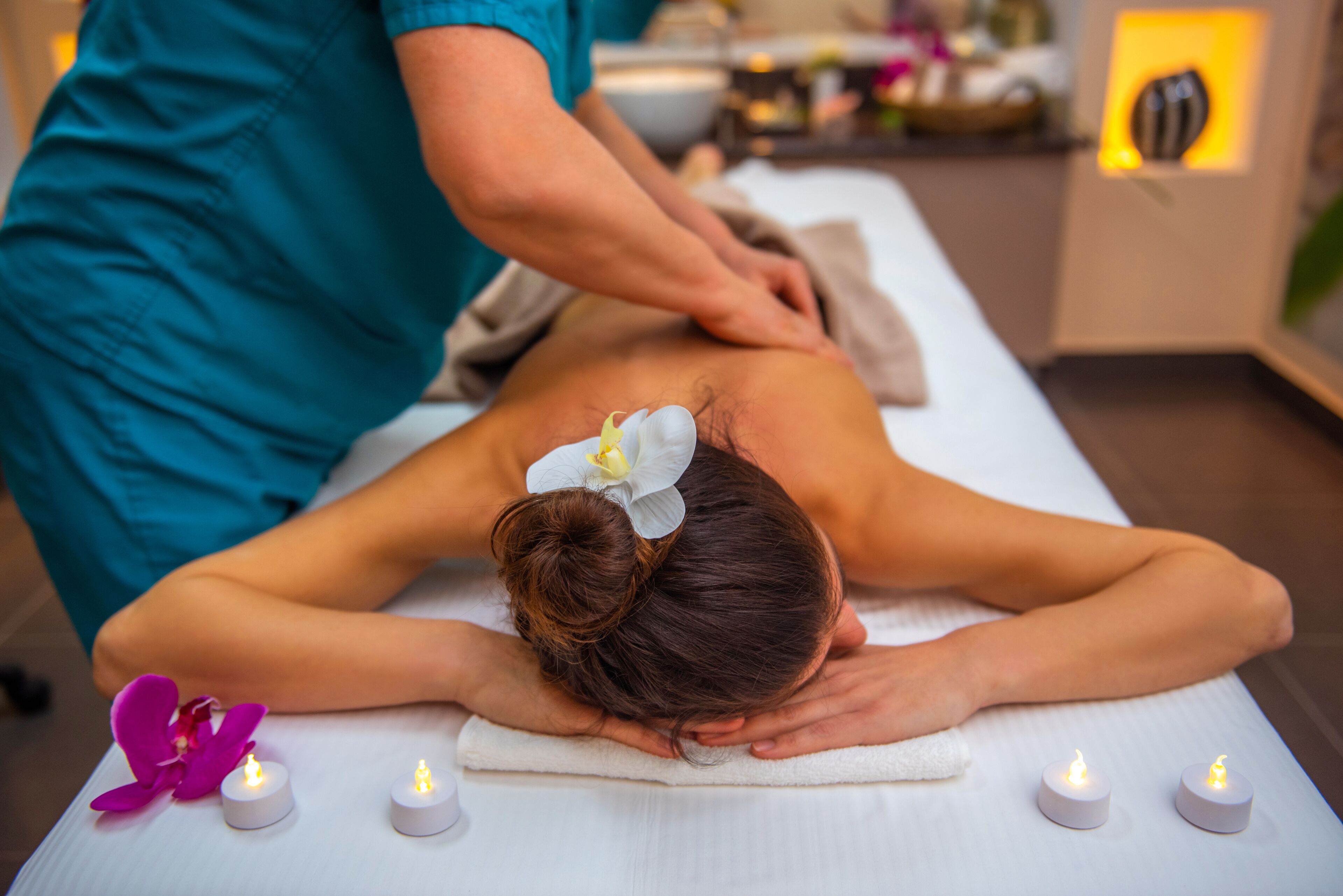 A massage therapy session in a spa setting with a massage table, candles, and decorative flowers.
