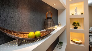 A modern interior with a woven basket containing two apples on a white shelf, a textured wall, and illuminated shelves with decorative items.