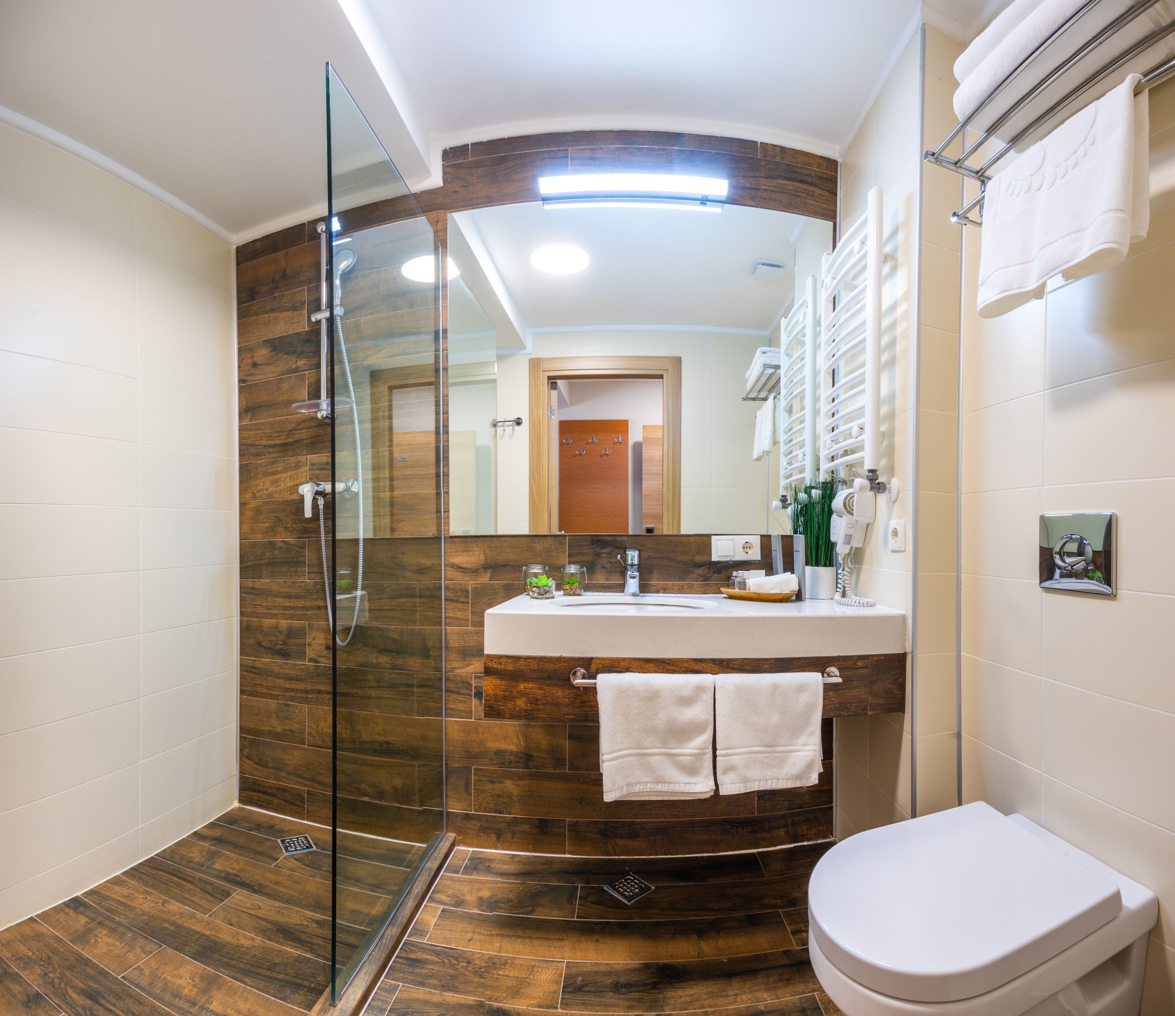 A modern bathroom with a glass-enclosed shower, a wooden vanity, and a white toilet.