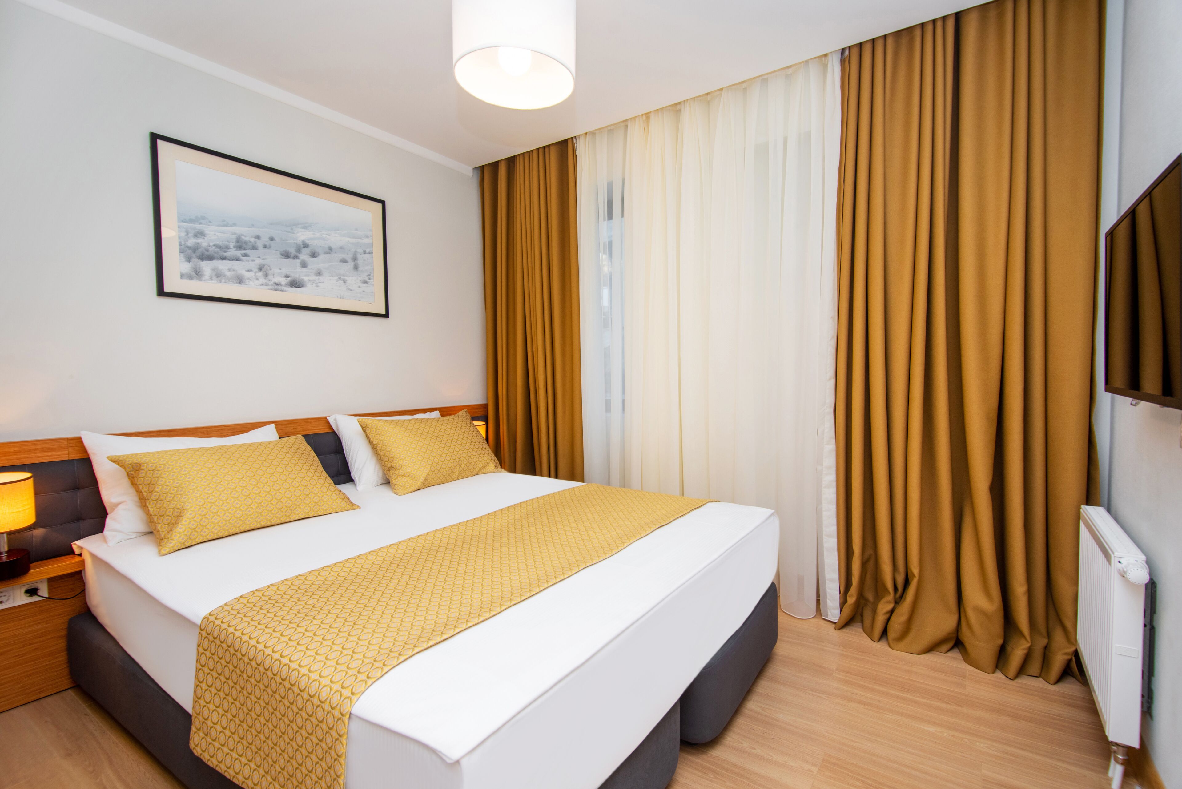 Habitación de hotel con una cama grande, una mesita de noche con lámpara, un cuadro enmarcado en la pared y cortinas.