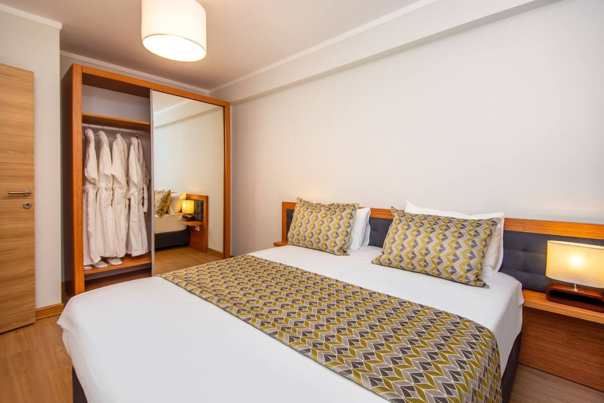 A hotel room with a large bed, a wardrobe, and a bedside table with a lamp.