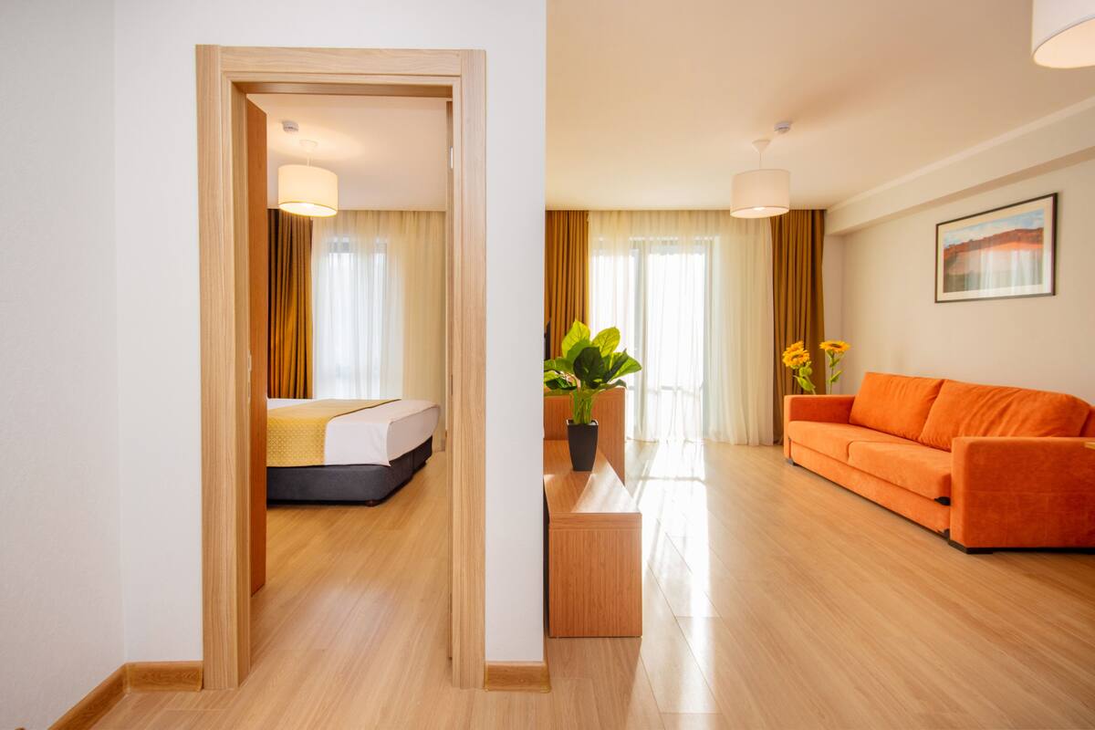 A hotel room with a bed, a wooden floor, a sofa, and a potted plant.