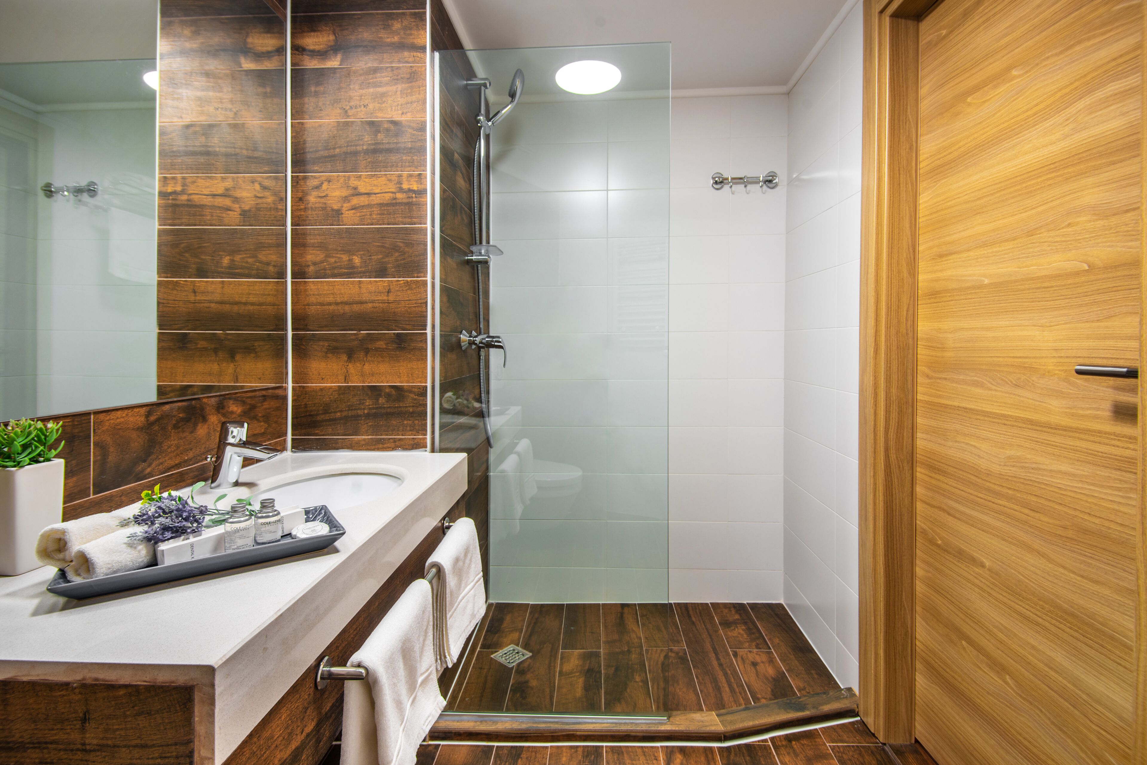 A modern bathroom with a wooden vanity, a glass shower enclosure, and a wooden door.