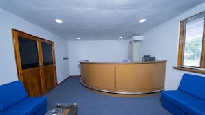 A reception area with a wooden reception desk, two blue sofas, a glass coffee table, and a wooden wardrobe. - Havana Club Resort (Trincomalee)