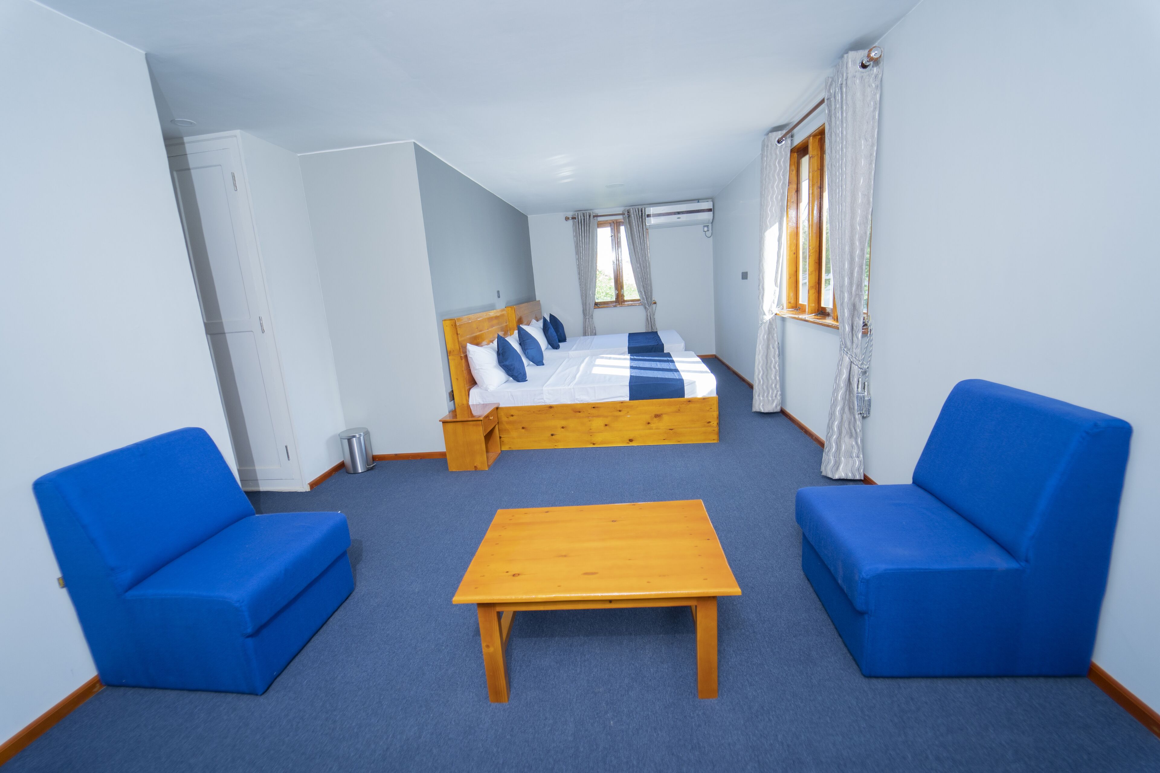A room with a bed, two blue sofas, a wooden table, and a window with curtains.