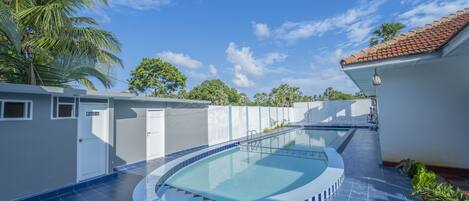 A swimming pool with a curved edge, surrounded by a white wall and a blue-tiled floor.