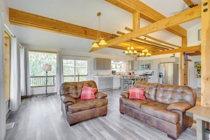 A spacious living area with leather sofas, a wooden ceiling, and a kitchen in the background.