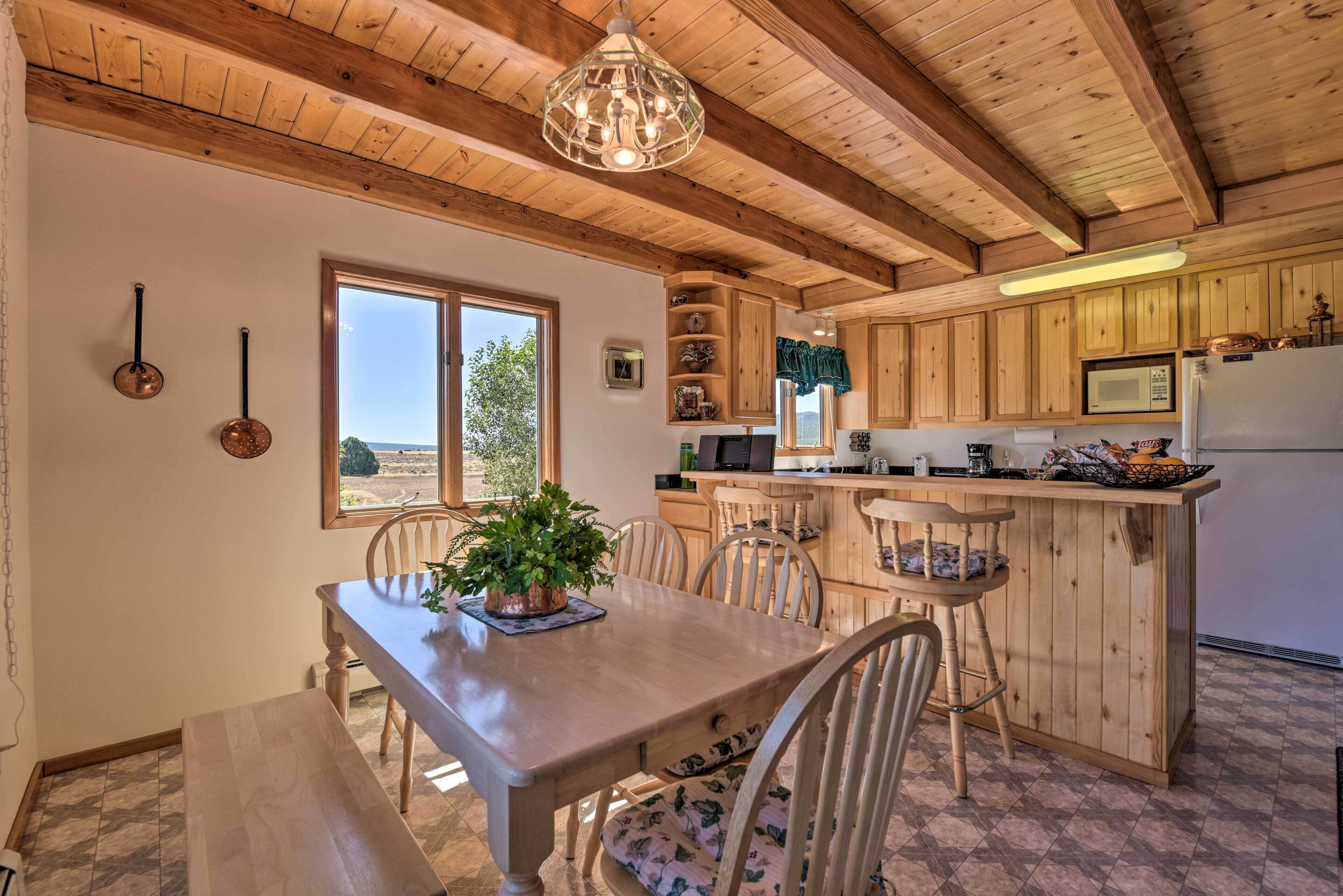 Un intérieur en bois comprenant une table à manger, des chaises, une plante en pot et un coin cuisine avec des meubles et des appareils électroménagers en bois.