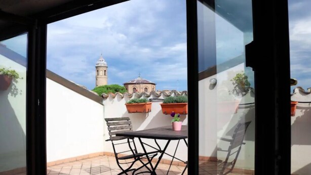 Ein Balkon mit Tisch und Stühlen, Blumentöpfen und Blick auf ein Gebäude mit einem Turm.