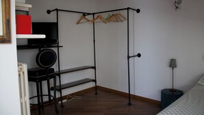 Ein Schlafzimmer mit einem Bett, einem Nachttisch, einer Lampe, einem Fernseher auf einem Regal, einem Kleiderständer und einem Stuhl.