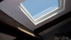 Ein Dachfenster in einem Raum mit sichtbaren Holzbalken und einem Topfpflanzen.
