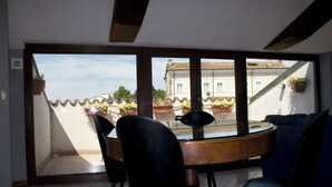 Ein Essbereich mit einem runden Tisch und Stühlen, großen Fenstern mit Blick auf Gebäude und Blumentöpfen am Fensterbrett.