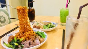 A table with two plates of food, one with noodles and meat, and another with noodles and vegetables. There are also two drinks, one dark and one green. - Dream Countryside Villa (Siem Reap)