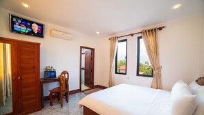 A hotel room with a bed, a desk with a laptop, a TV mounted on the wall, and a window with curtains. - Dream Countryside Villa (Siem Reap)