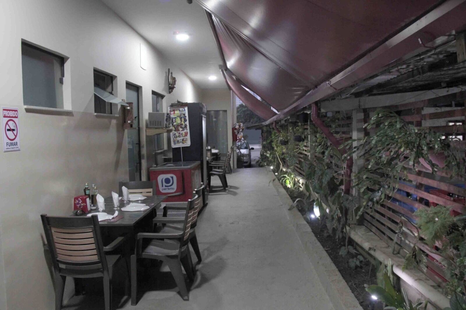 Un restaurante con una barra larga, sillas y un refrigerador. Hay un cartel que prohíbe fumar y una ventana pequeña en la pared.