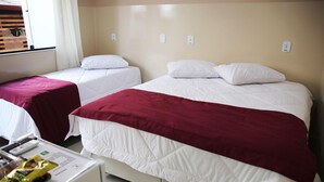 A hotel room with two single beds, one with a red blanket and the other with a white blanket. There is a small table with a remote control and a snack packet. - Hotel Malbec (Aparecida)