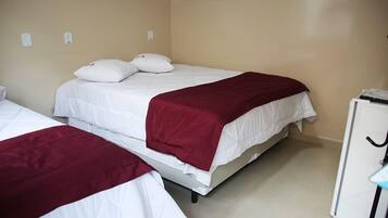 Quarto de hotel com duas camas de solteiro, cada uma com roupa de cama branca e manta vermelha. Há um armário branco com puxador preto no lado direito.