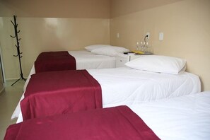A hotel room with three single beds, each with white bedding and a red blanket. There is a bedside table with a lamp and a fruit bowl. - Hotel Malbec (Aparecida)