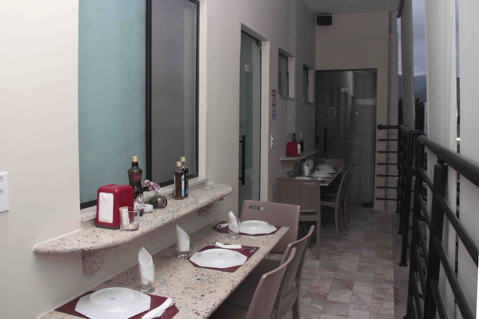 Un pasillo estrecho con una zona de cocina a la derecha, que incluye una mesa de comedor con platos y vasos, y una encimera con botellas y un electrodoméstico rojo.