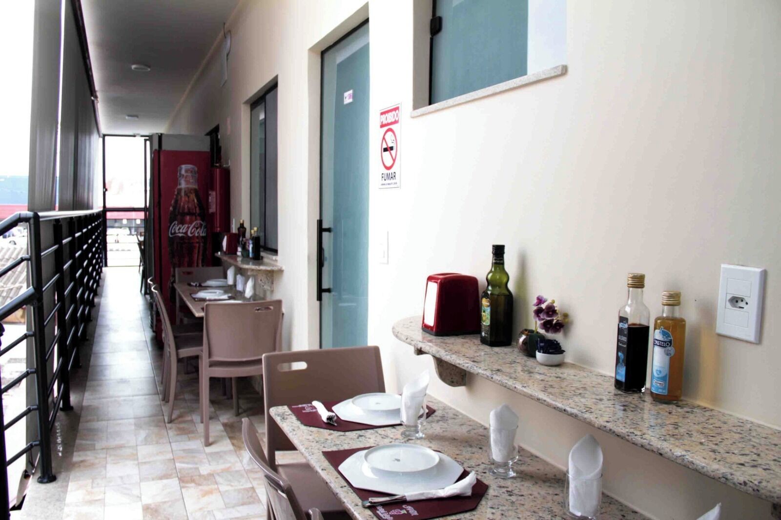 A corridor with a dining area featuring tables set with plates and napkins, a red toaster, and various bottles on a counter.