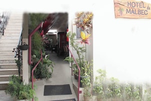 Entrada de un hotel con una escalera que conduce a un área cubierta, rodeada de plantas en macetas y un letrero que dice 'HOTEL MALBEC'.